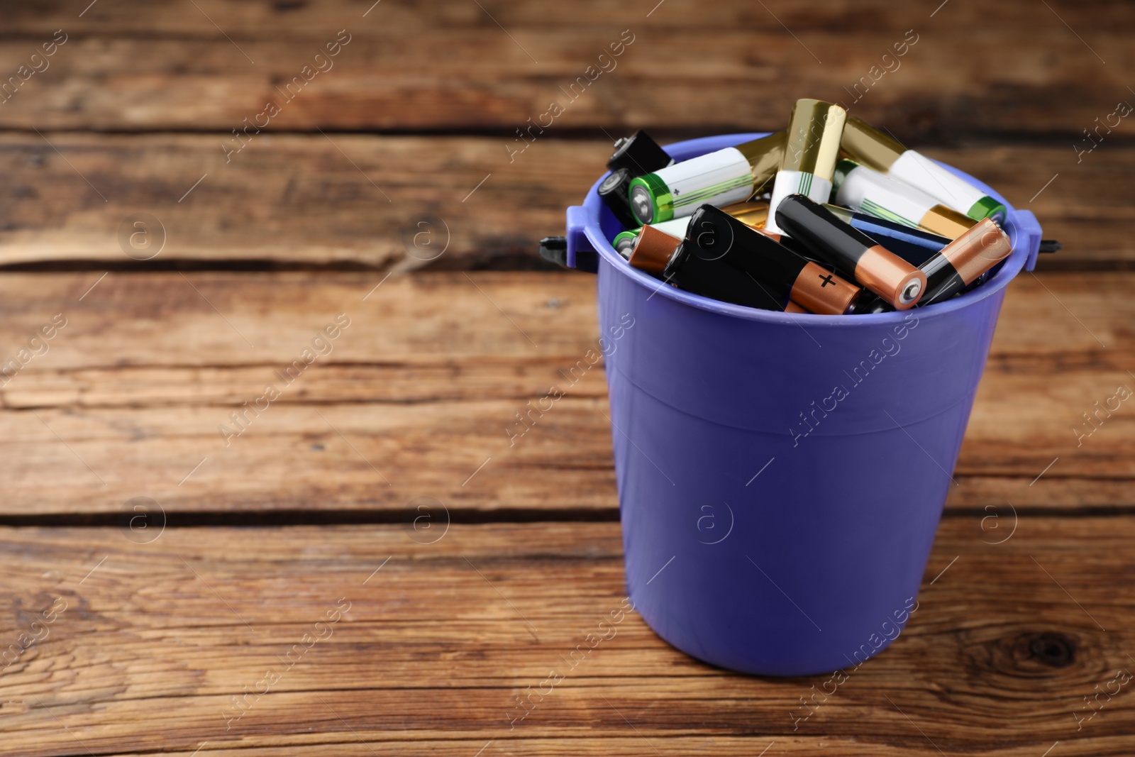 Image of Used batteries in bucket on wooden table, space for text