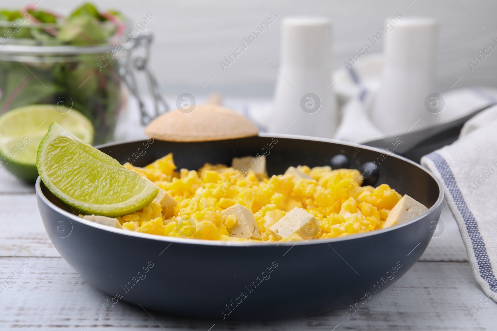 Photo of Frying pan with delicious scrambled eggs, tofu and lime on white wooden table