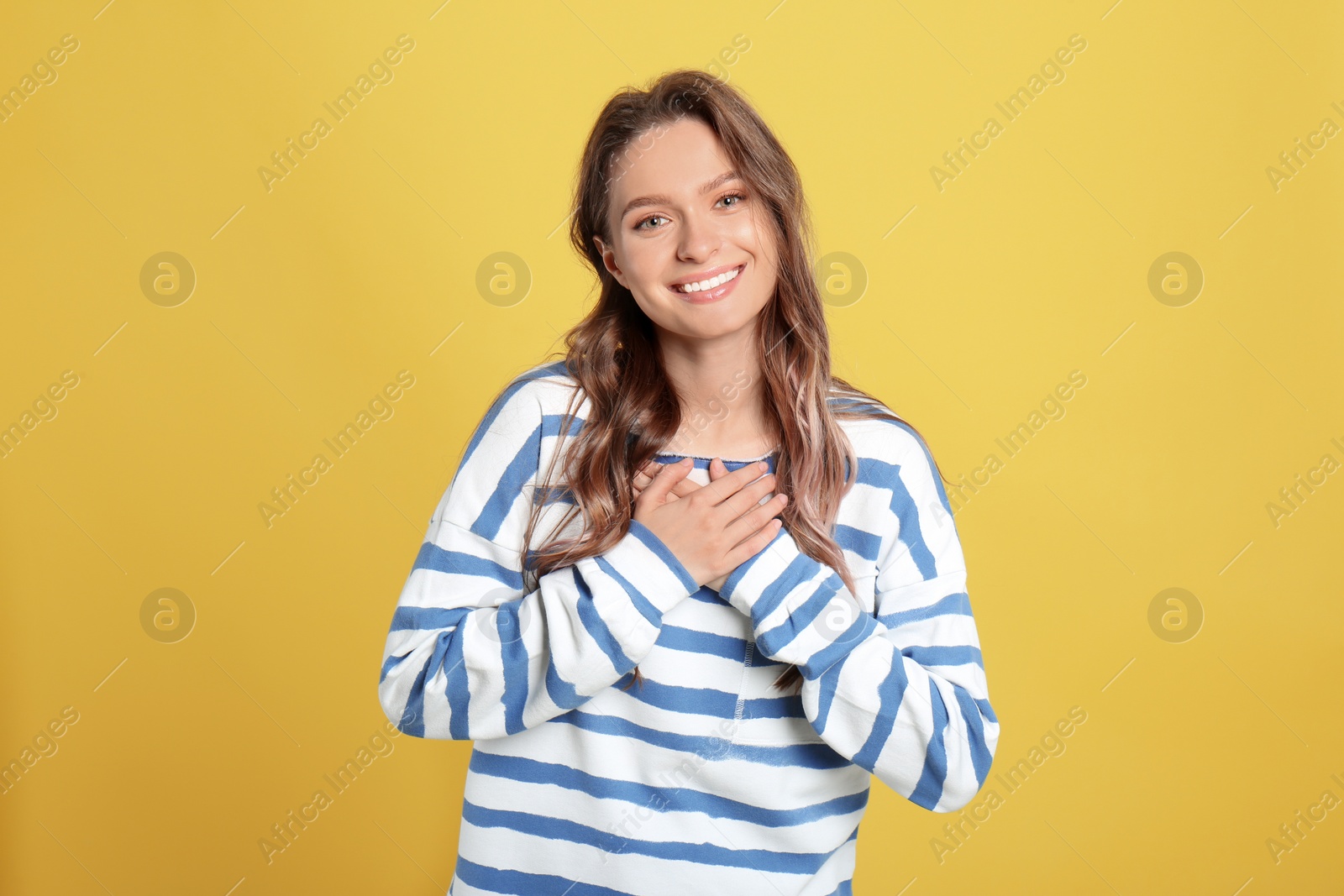 Photo of Beautiful grateful woman with hands on chest against yellow background