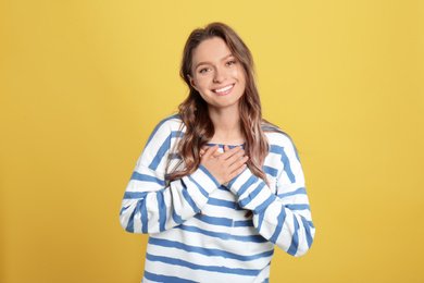 Beautiful grateful woman with hands on chest against yellow background