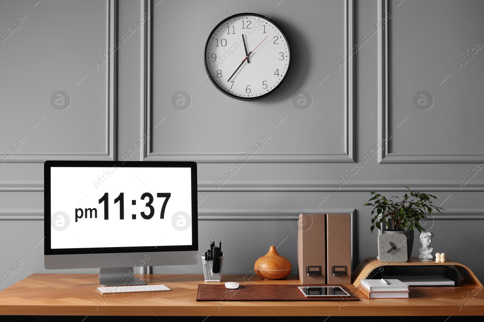 Photo of Stylish workplace with computer, houseplant and stationery on wooden desk near grey wall at home