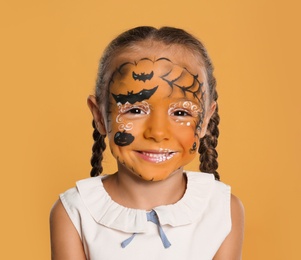 Photo of Cute little girl with face painting on orange background