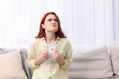 Angry woman popping bubble wrap on sofa at home, space for text. Stress relief