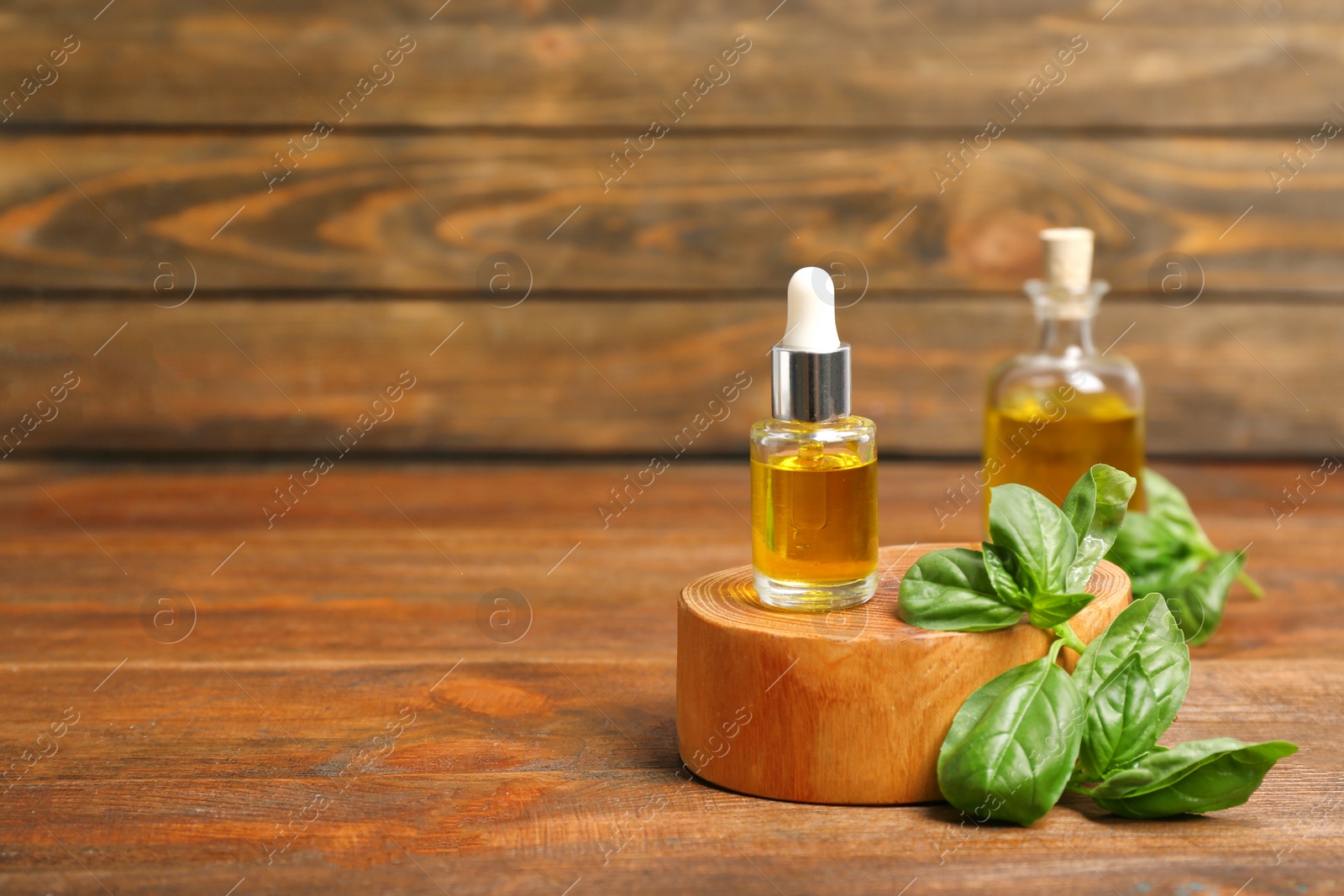 Photo of Glass bottle of oil with basil leaves on wooden table. Space for text