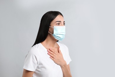 Young woman with protective mask suffering from breathing problem on light background