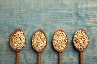 Uncooked green buckwheat grains in spoons on light blue wooden table, flat lay. Space for text