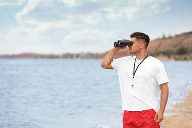 Photo of Handsome male lifeguard with binocular near sea