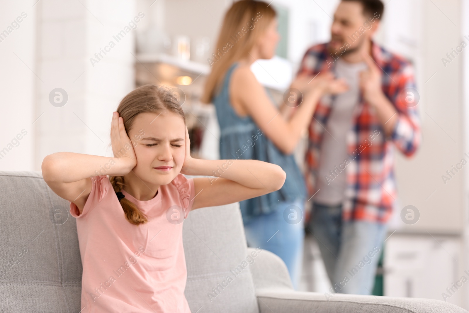 Photo of Little unhappy girl sitting on sofa while parents arguing at home