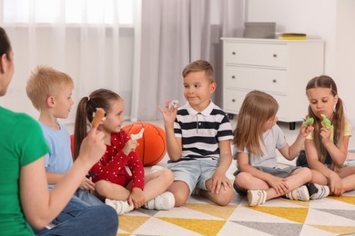 Photo of Nursery teacher and group of cute little children with finger toys for puppet show on bright rug in kindergarten. Playtime activities