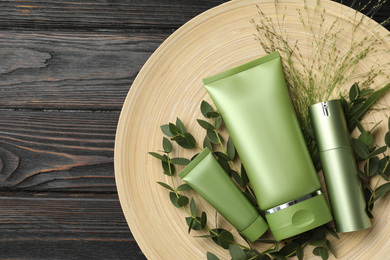 Set of cosmetic products and plants on dark wooden table, top view