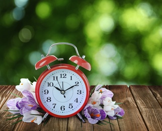 Image of Alarm clock and spring flowers on wooden table. Time change 