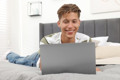 Happy young man having video chat via laptop on bed indoors