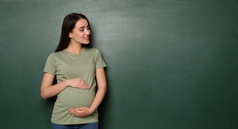 Pregnant woman near empty green chalkboard, space for text. Choosing name for baby