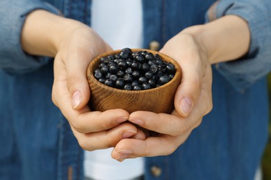 Woman holding wooden bowl of bilberries, closeup