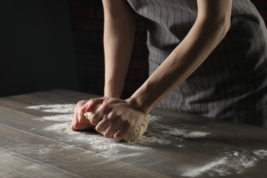 Photo of Making bread. Woman kneading dough at wooden table indoors, closeup