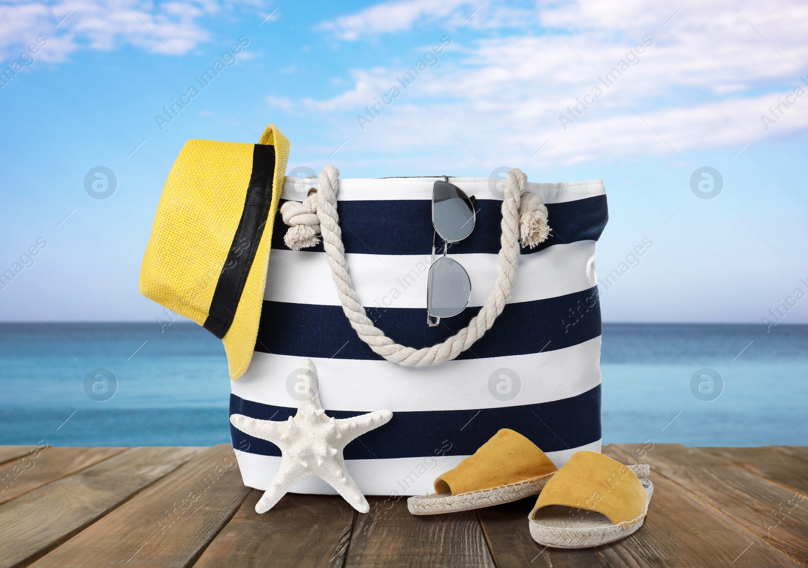 Image of Stylish bag with beach accessories on wooden surface near seashore