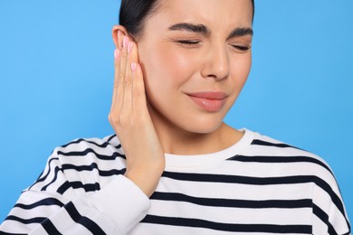 Photo of Young woman suffering from ear pain on light blue background, closeup