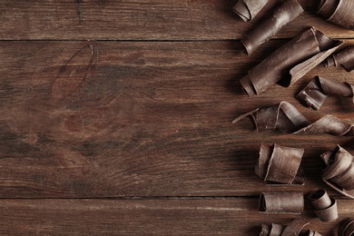 Photo of Yummy chocolate curls and space for text on wooden background, top view