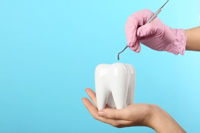 Dentist holding ceramic model of tooth and professional tool on color background, space for text
