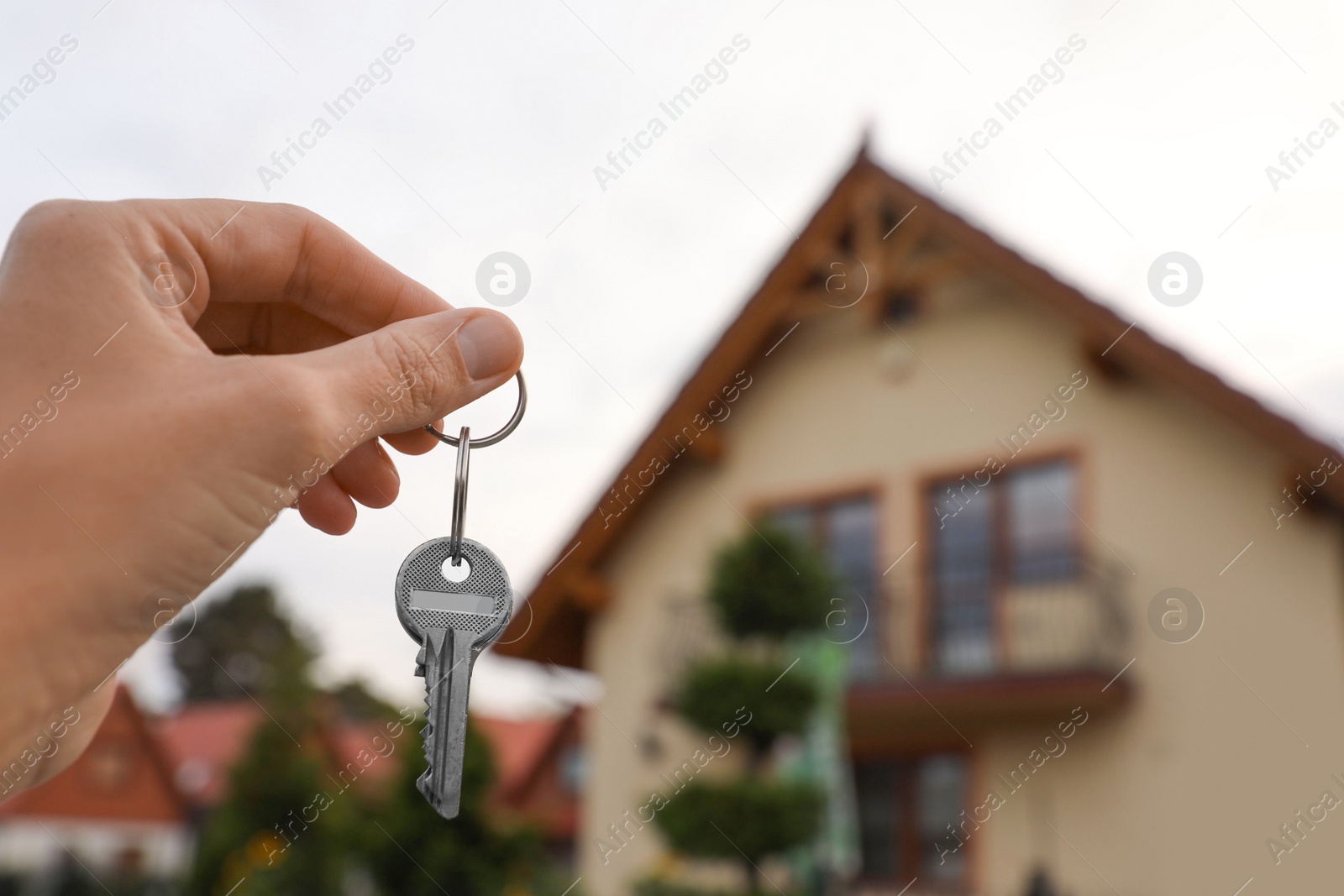 Photo of Real estate agent holding keys to new house outdoors, closeup. Space for text