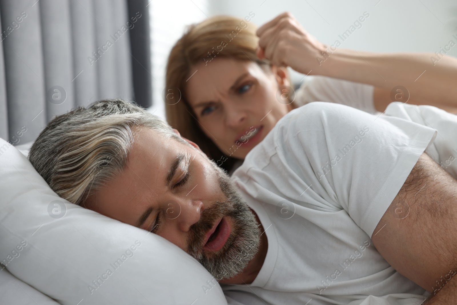 Photo of Irritated woman near her snoring husband in bed at home