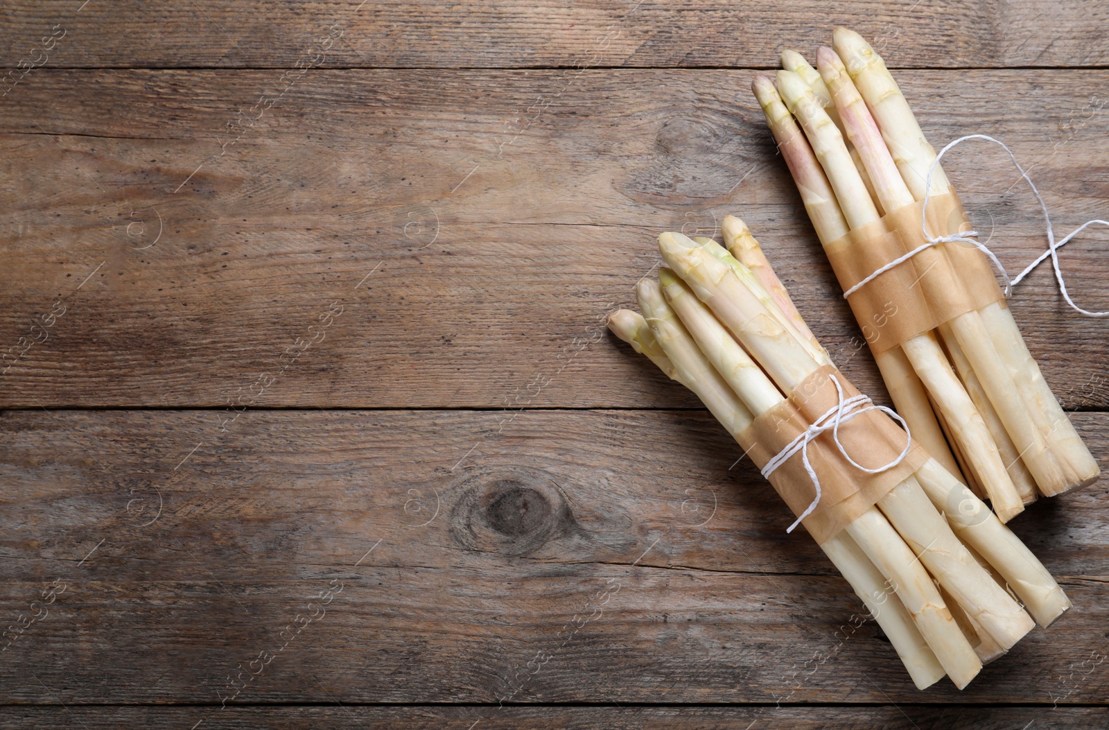 Photo of Bunches of fresh white asparagus on wooden table, flat lay. Space for text