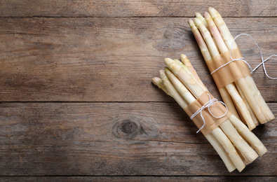 Photo of Bunches of fresh white asparagus on wooden table, flat lay. Space for text