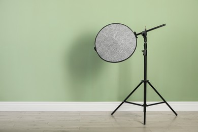 Studio reflector on tripod near pale green wall indoors, space for text. Professional photographer's equipment