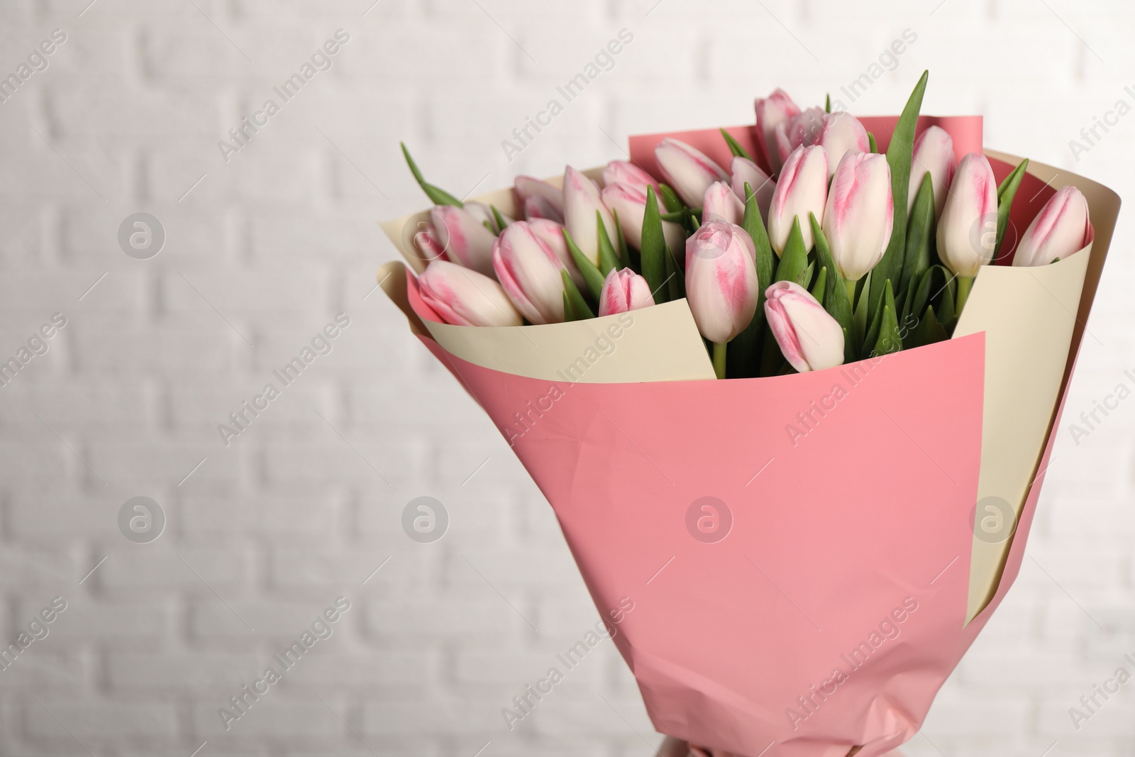 Photo of Beautiful bouquet of fresh pink tulips against white brick wall. Space for text