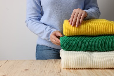 Photo of Woman with folded sweaters at wooden table on light background, closeup