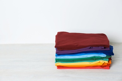 Photo of Stack of bright folded clothes on table against white background. Space for text