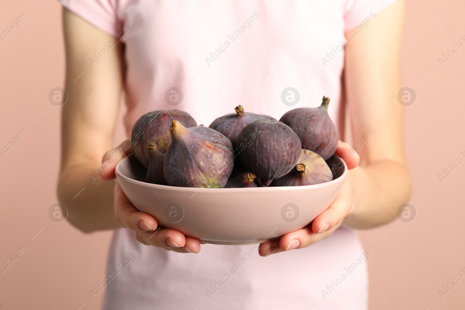 Photo of Woman holding bowl with tasty raw figs on pink  background, closeup