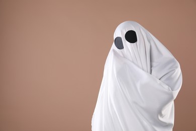 Photo of Creepy ghost. Person covered with white sheet on dark beige background, space for text