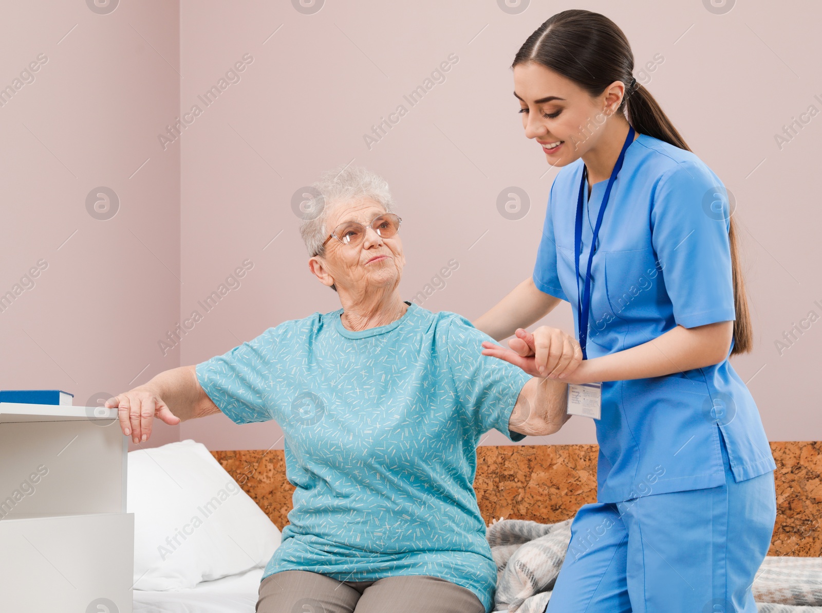 Photo of Nurse assisting senior woman on bed in hospital ward