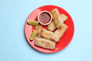 Photo of Tasty fried spring rolls, lime and sauce on light blue table, top view