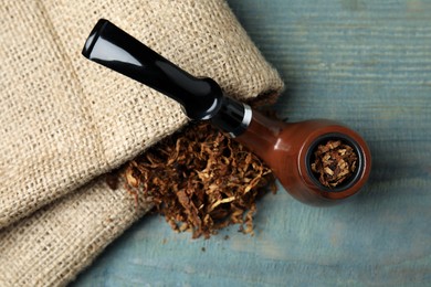 Photo of Smoking pipe, dry tobacco and sackcloth on blue wooden table, top view