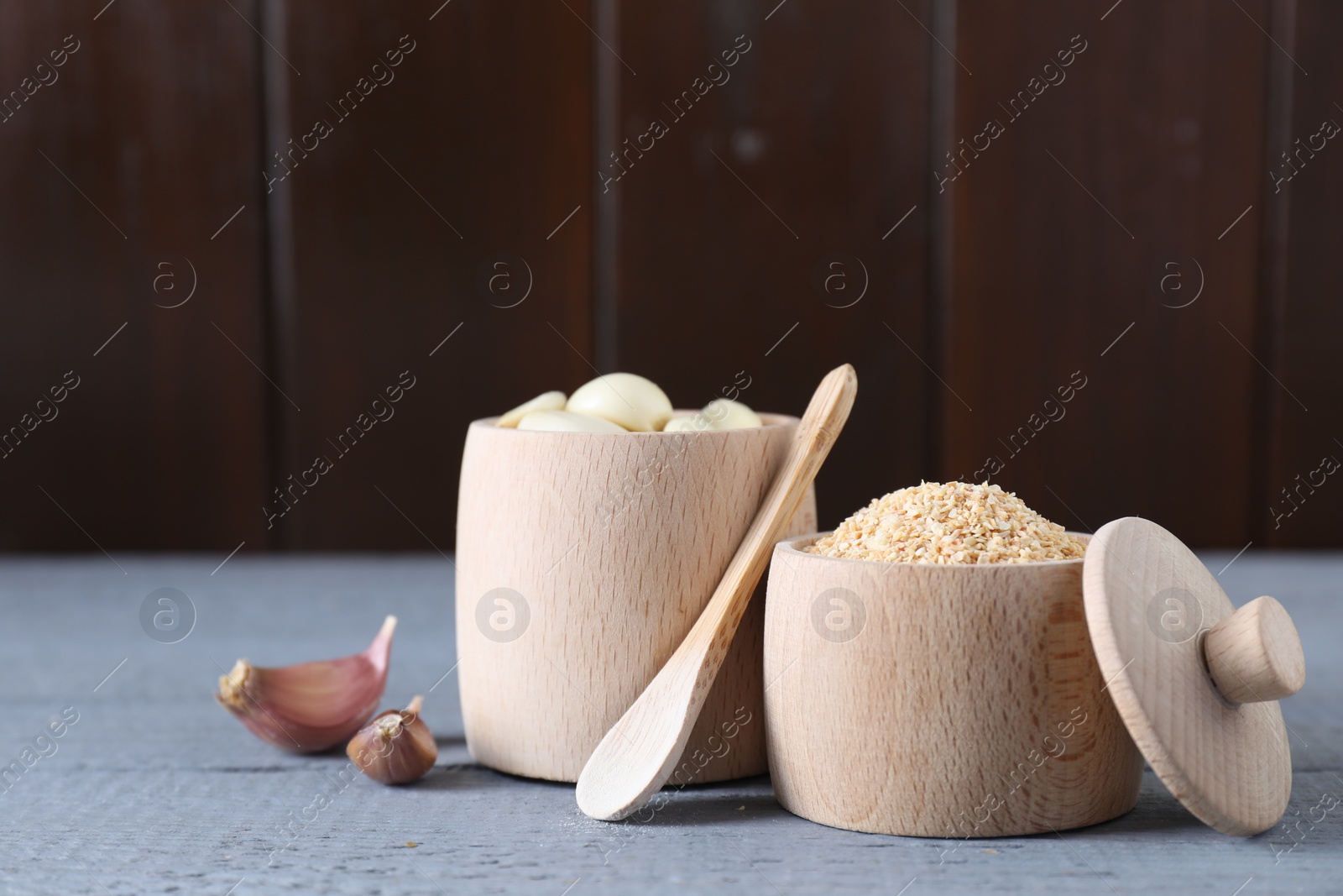 Photo of Dehydrated garlic granules, fresh cloves and spoon on grey wooden table. Space for text