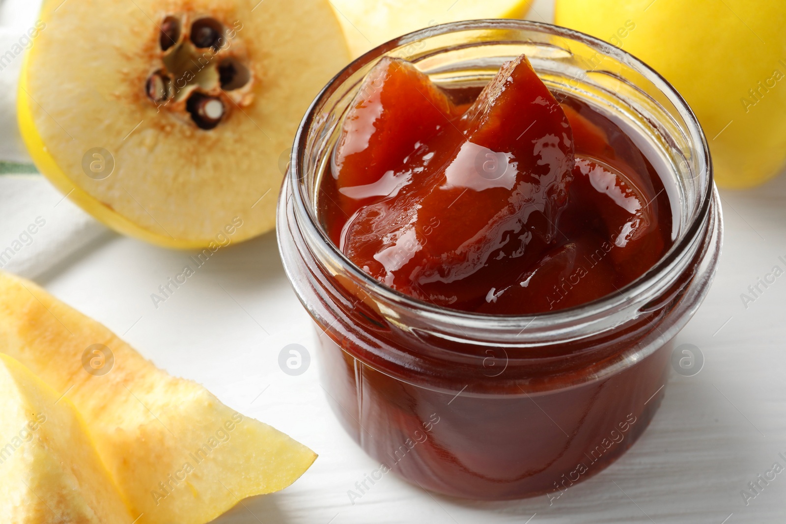 Photo of Tasty homemade quince jam in jar and fruits on white wooden table, closeup