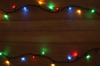 Frame of colorful Christmas lights on wooden table, top view. Space for text