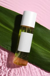 Photo of Bottle of cosmetic oil with green leaf in water on pink background, flat lay