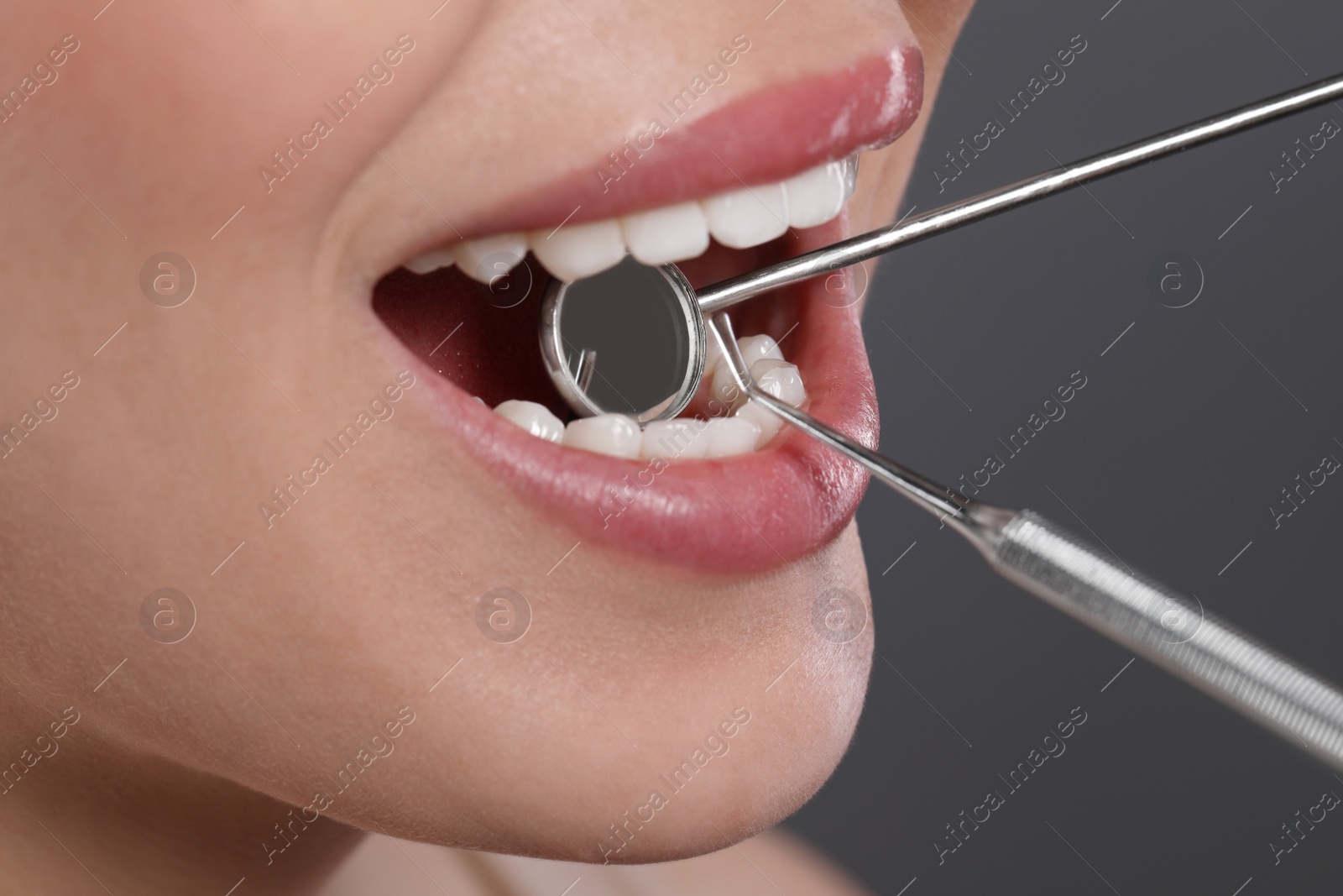 Photo of Examining woman's teeth with dentist's mirror on grey background, closeup