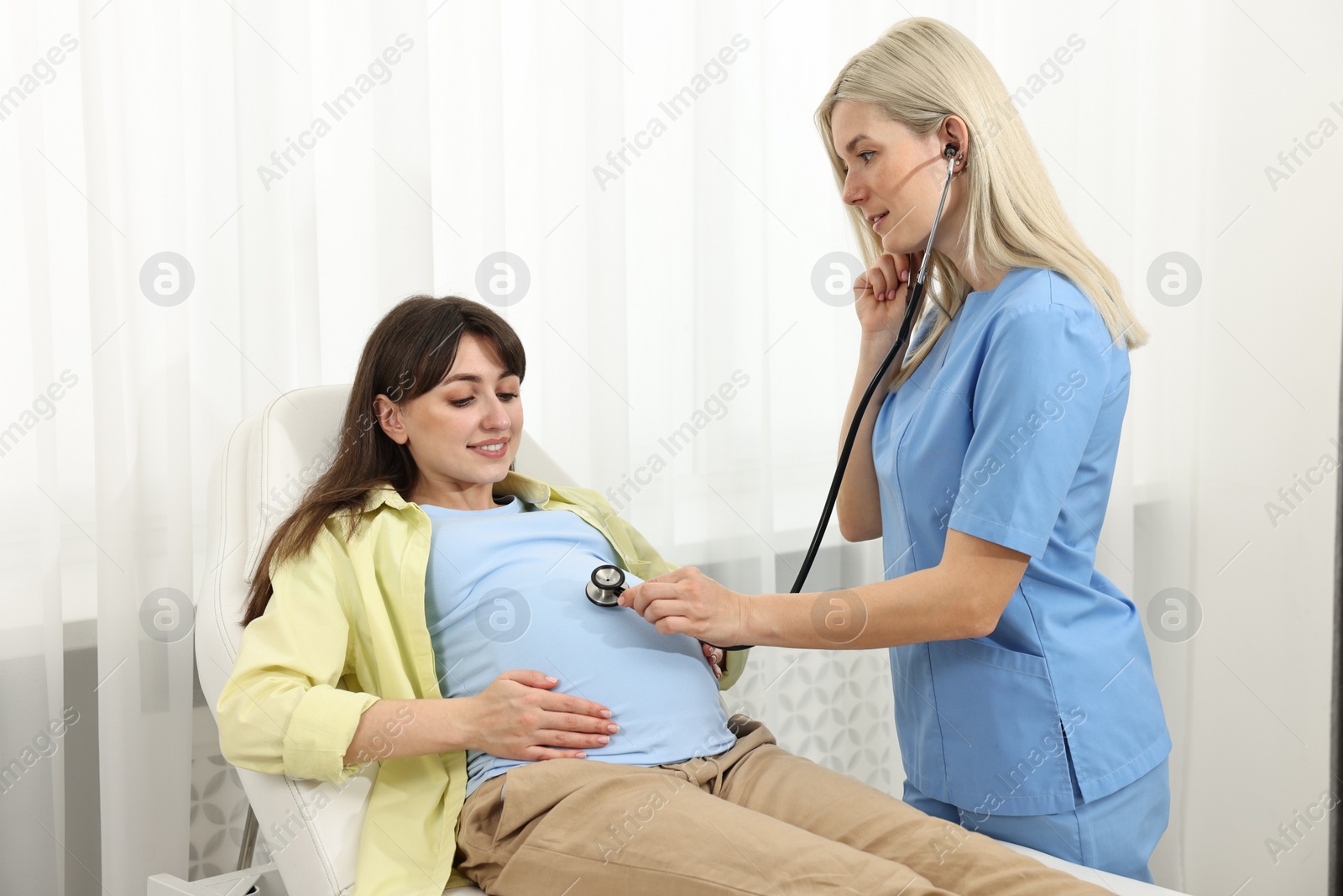 Photo of Pregnancy checkup. Doctor with stethoscope listening baby's heartbeat in patient's tummy in clinic