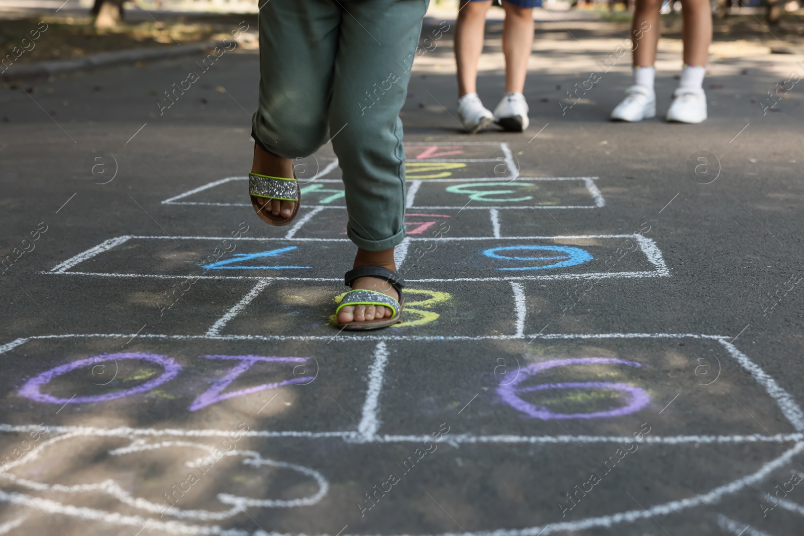 Photo of Little African American girl playing hopscotch drawn with chalk on asphalt outdoors, closeup. Happy childhood