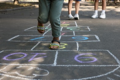 Photo of Little African American girl playing hopscotch drawn with chalk on asphalt outdoors, closeup. Happy childhood