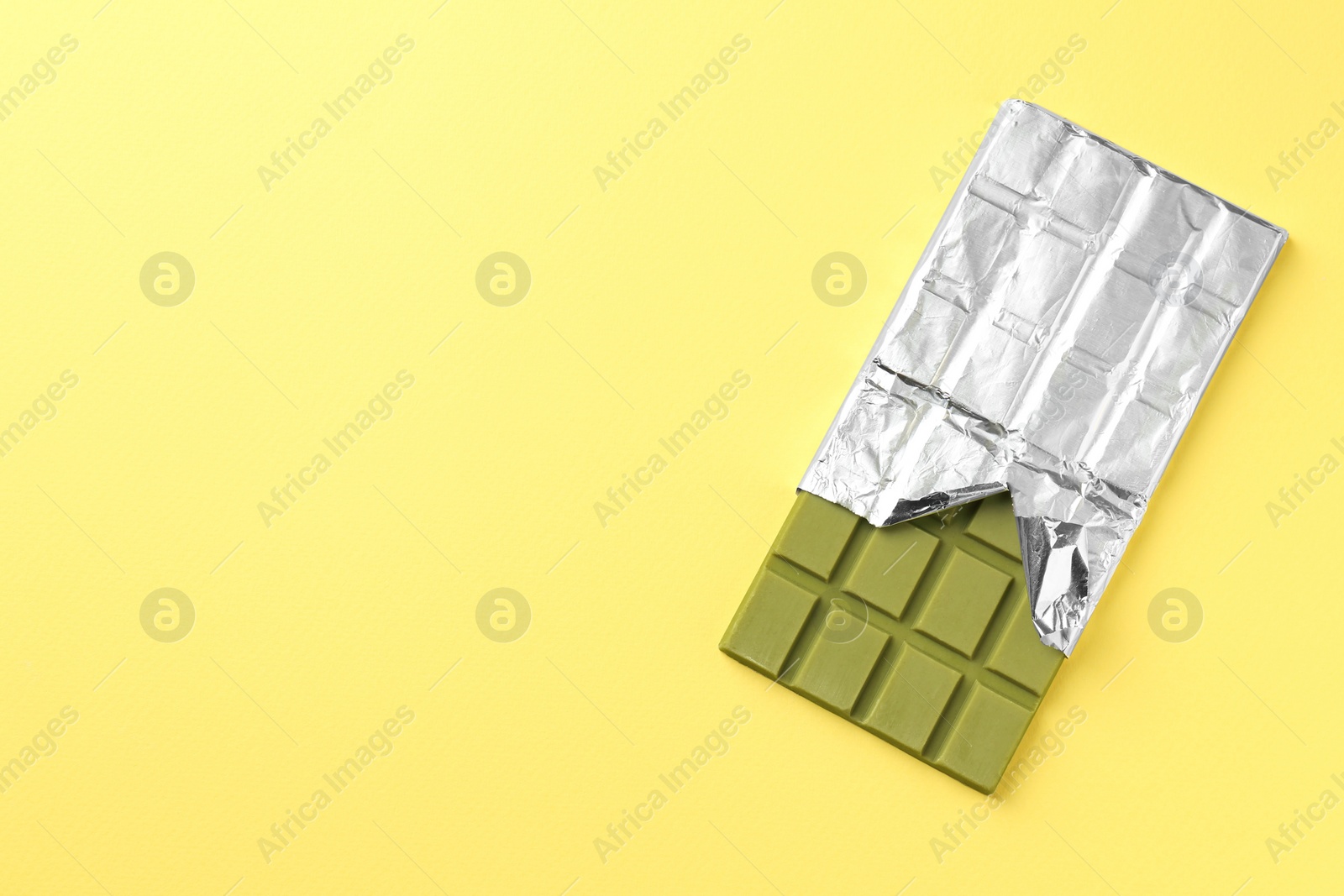 Photo of Tasty matcha chocolate bar wrapped in foil on yellow background, top view. Space for text