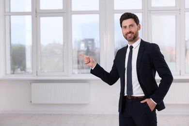 Photo of Happy real estate agent pointing in new apartment. Space for text