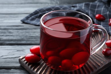 Glass cup of fresh dogwood tea with berries on black wooden table, closeup