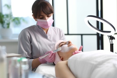 Photo of Cosmetologist applying mask on woman's face in clinic