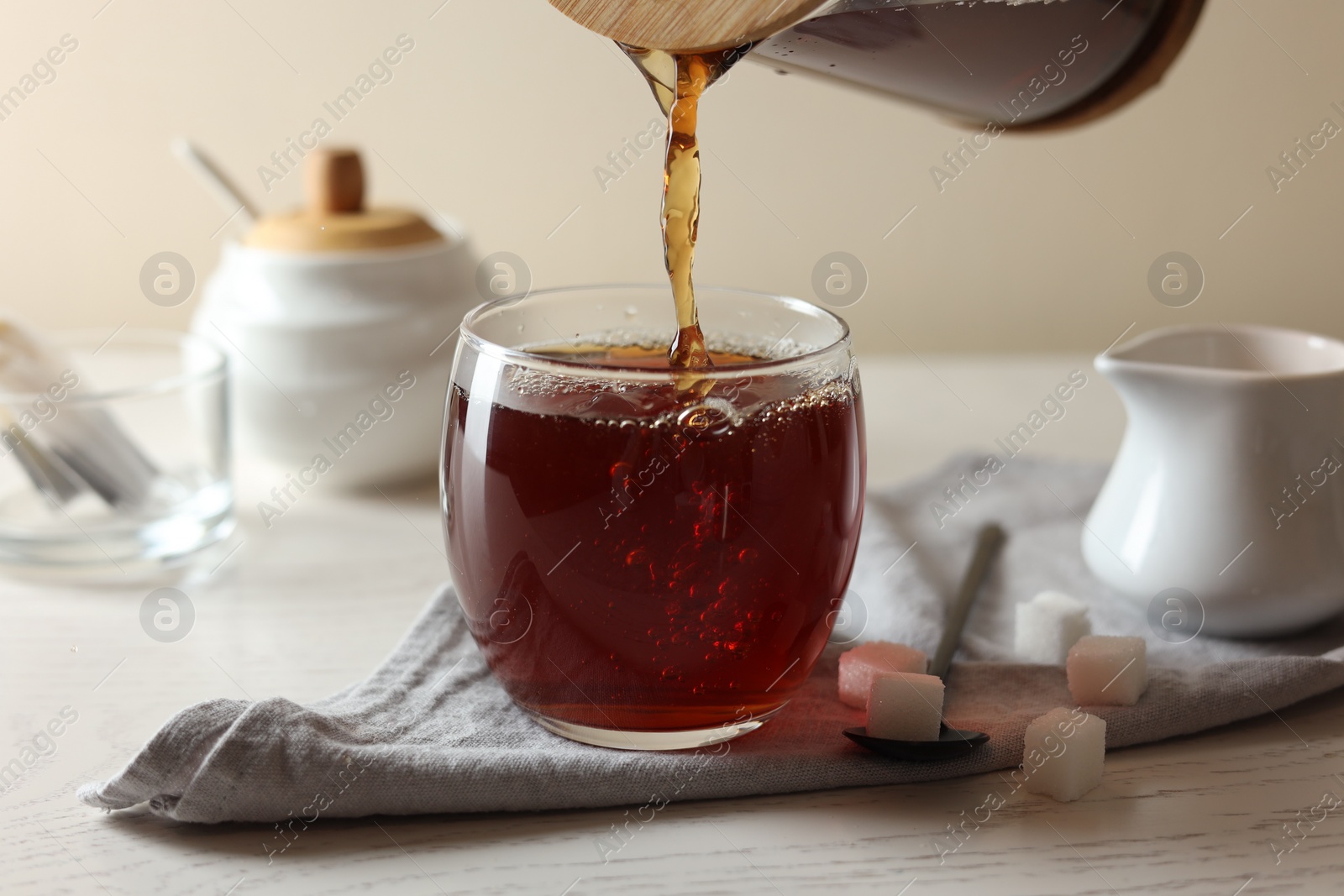 Photo of Pouring warm tea into cup on white wooden table, closeup