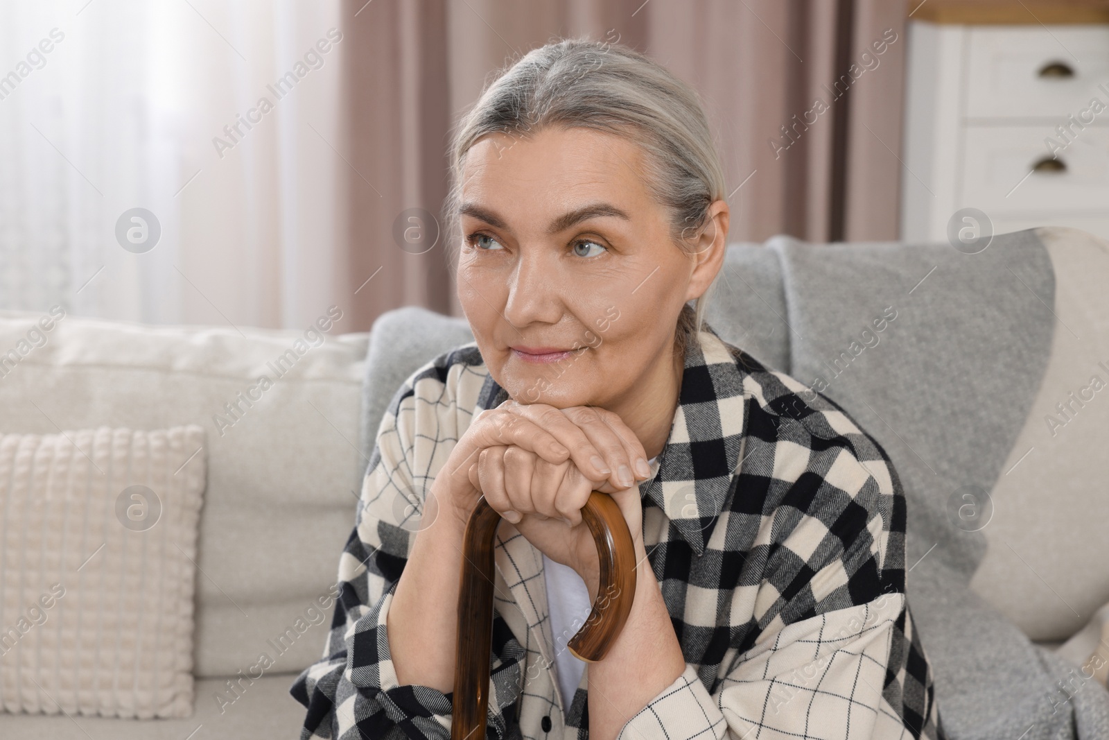 Photo of Senior woman with walking cane sitting on sofa at home